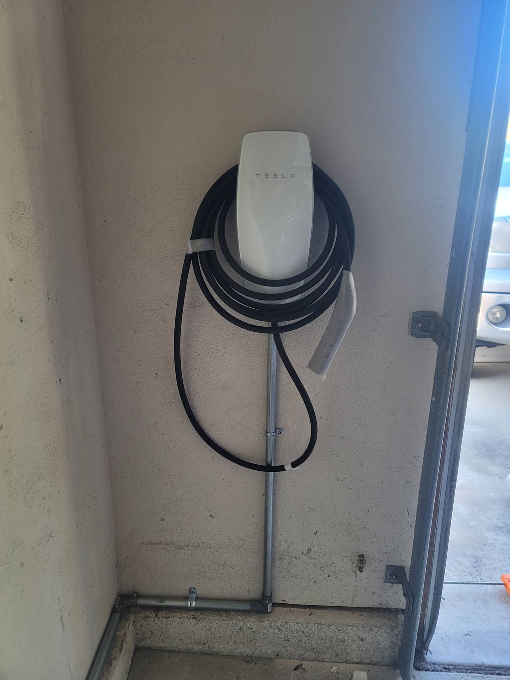Finished EV charger installation showing the protected conduit run along the garage wall